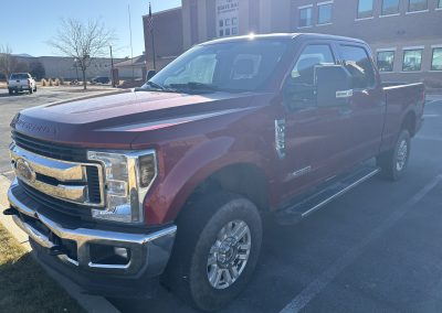 Red Ford pickup truck parked in a lot near a brick building.