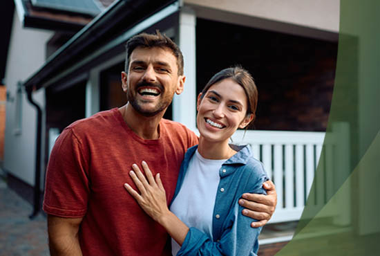 home-owners-rate-advantage young couple standing in front of a house smiling